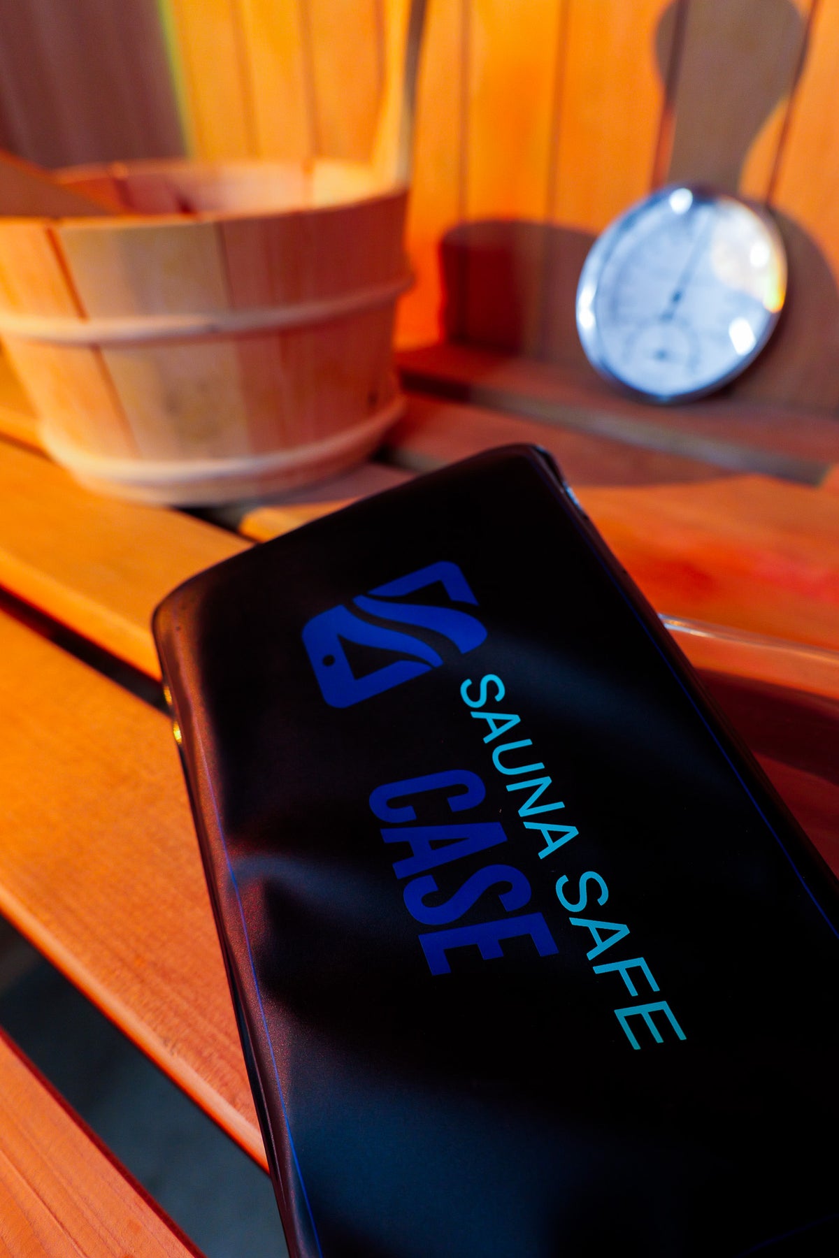 Sauna Safe Case on a cedar sauna bench next to a wooden bucket and thermometer